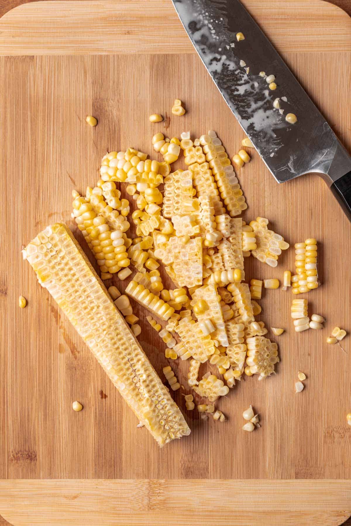 Corn kernels on a cutting board next to a cob with all the kernels cut off.