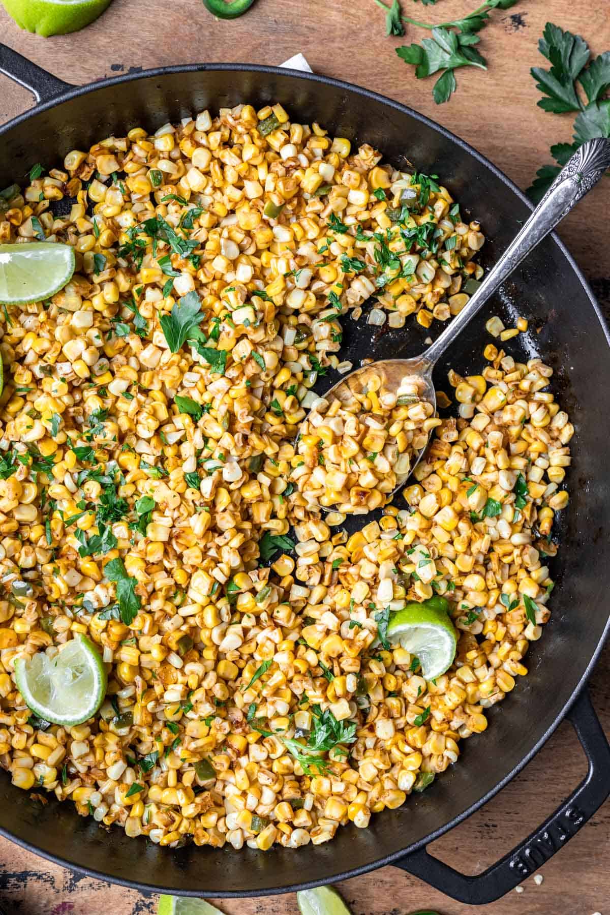 Seasoned corn in a cast iron skillet with a serving spoon.