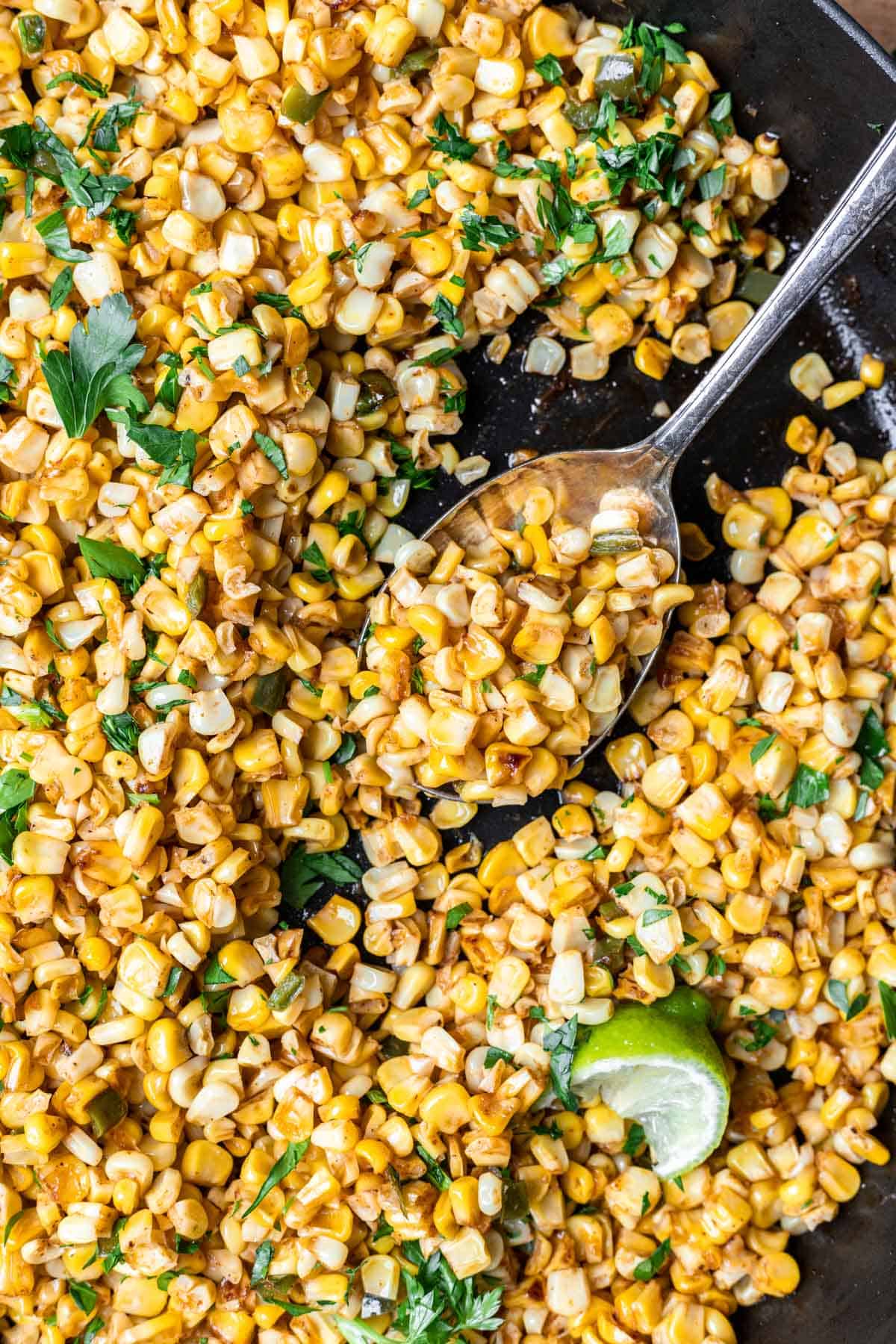 Skillet roasted corn getting scooped up by a serving spoon.