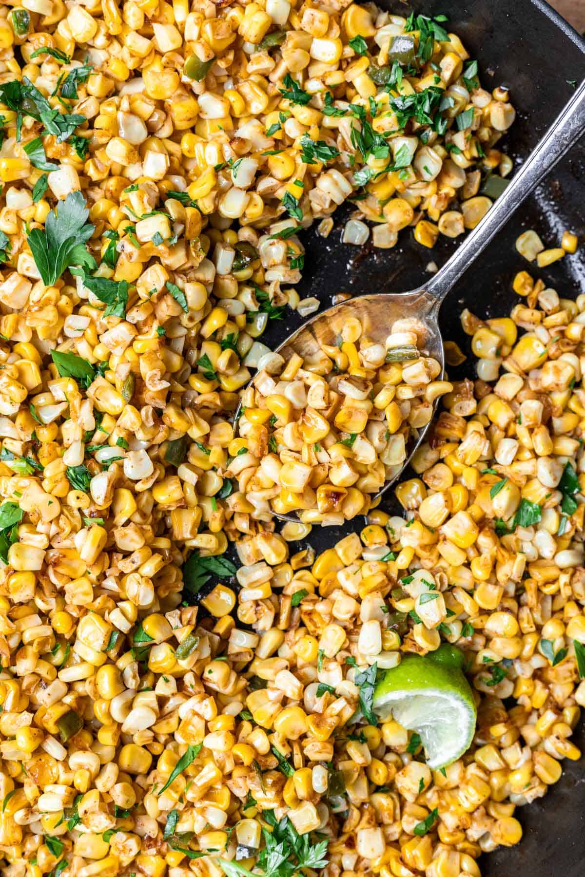Skillet roasted corn getting scooped up by a serving spoon.
