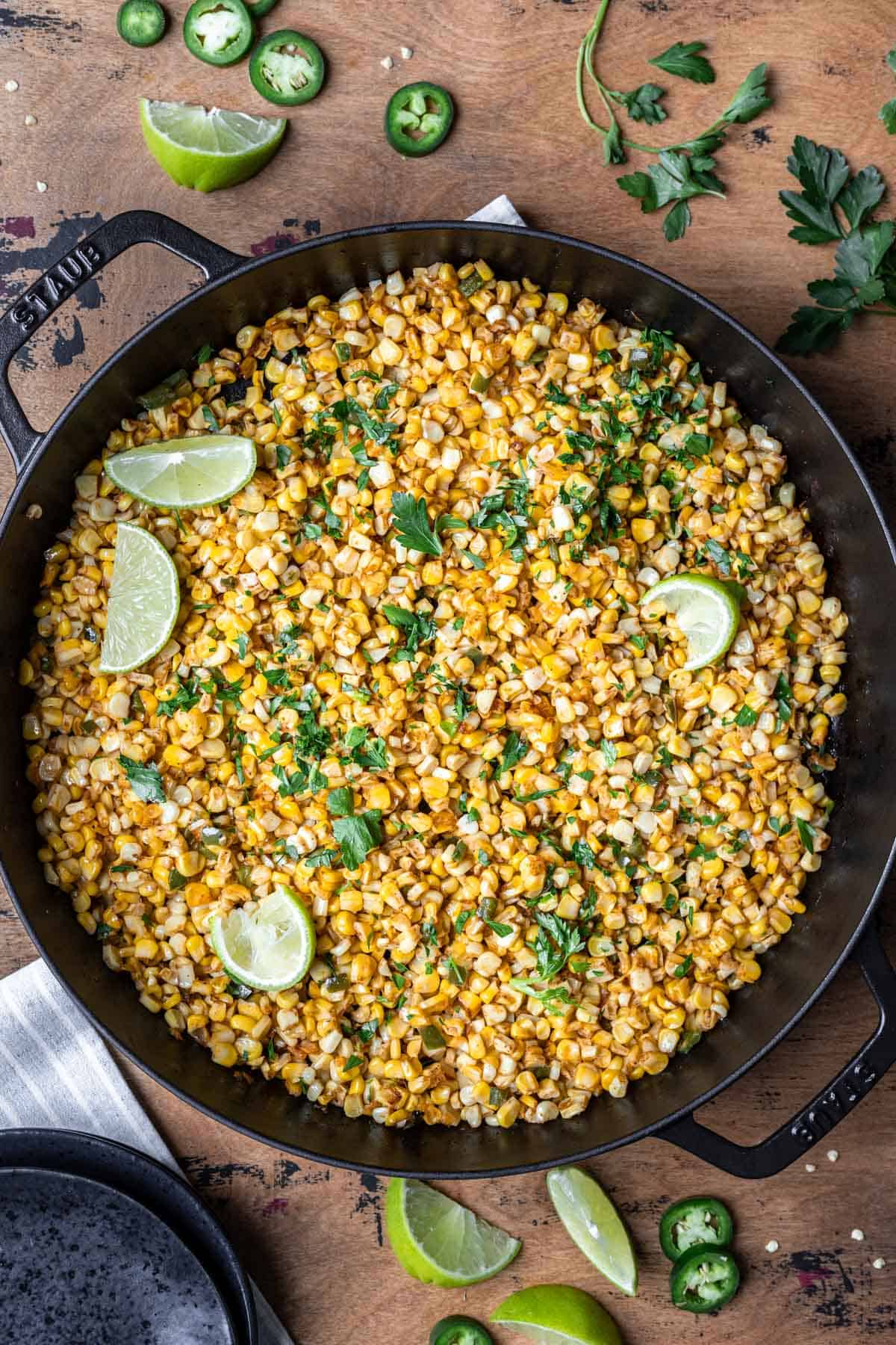 Roasted corn kernels in a cast iron skillet topped with fresh parsley and lime wedges.