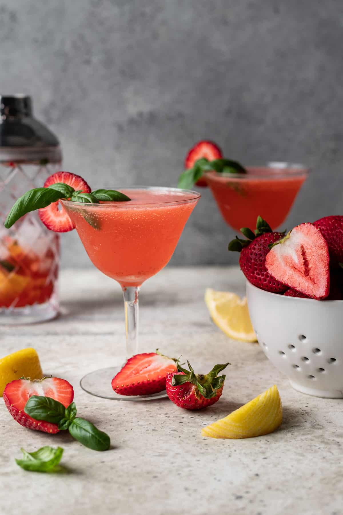 Strawberry basil gin smash surrounded by lemon wedges and sliced strawberries.