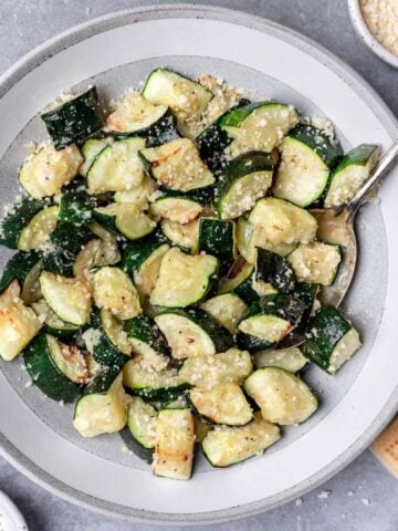 Air fryer zucchini in a serving bowl with a spoon.