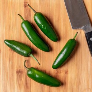 Jalapeños with a knife on a wood cutting board.