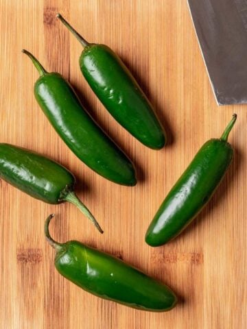 Jalapeños with a knife on a wood cutting board.