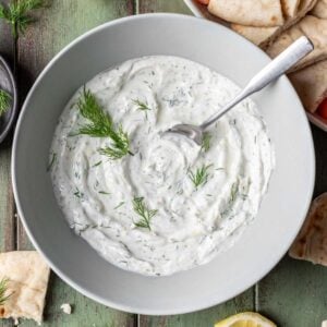 Lemon dill yogurt sauce in a serving bowl with pita and vegetables next to it.