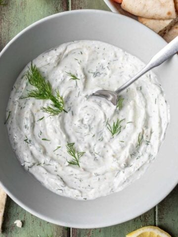 Lemon dill yogurt sauce in a serving bowl with pita and vegetables next to it.