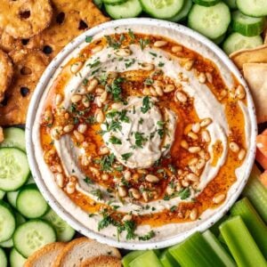 Pine nut hummus on a serving platter with fresh vegetables, pretzels, and chips.