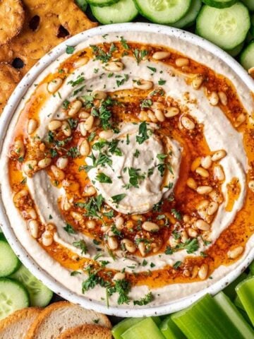 Pine nut hummus on a serving platter with fresh vegetables, pretzels, and chips.