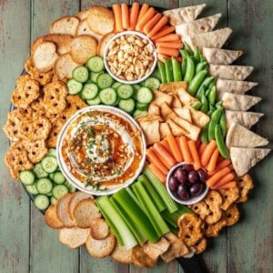 A large snack tray with hummus, vegetables, nuts, olives, and chips.