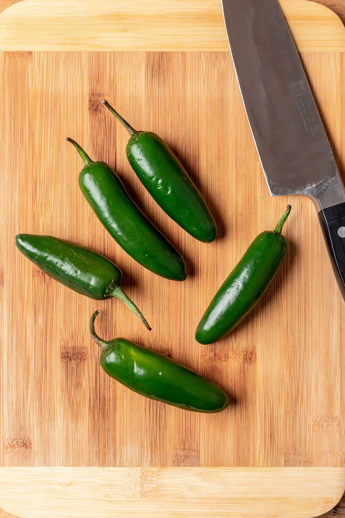 5 jalapeños on a wood cutting board with a knife.