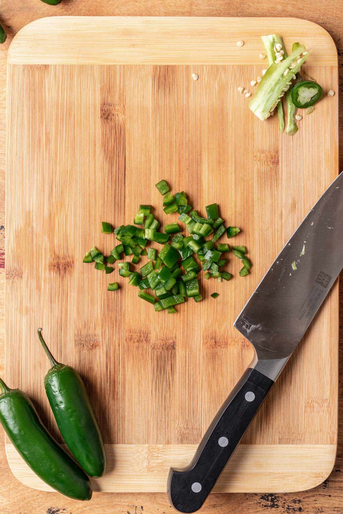 Minced jalapeño in the center of a wood cutting board.