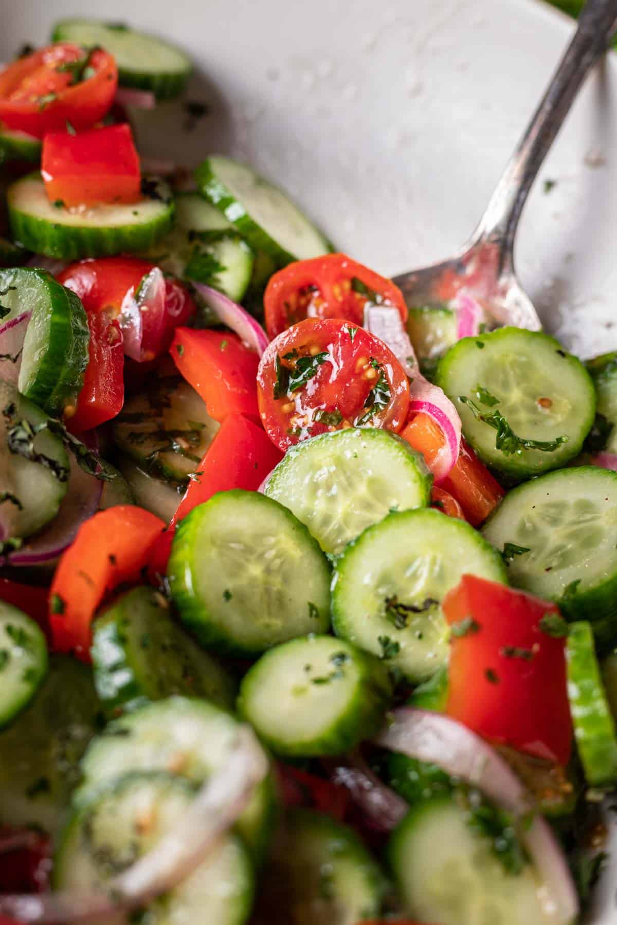 Israeli salad in a white bowl with a serving spoon.