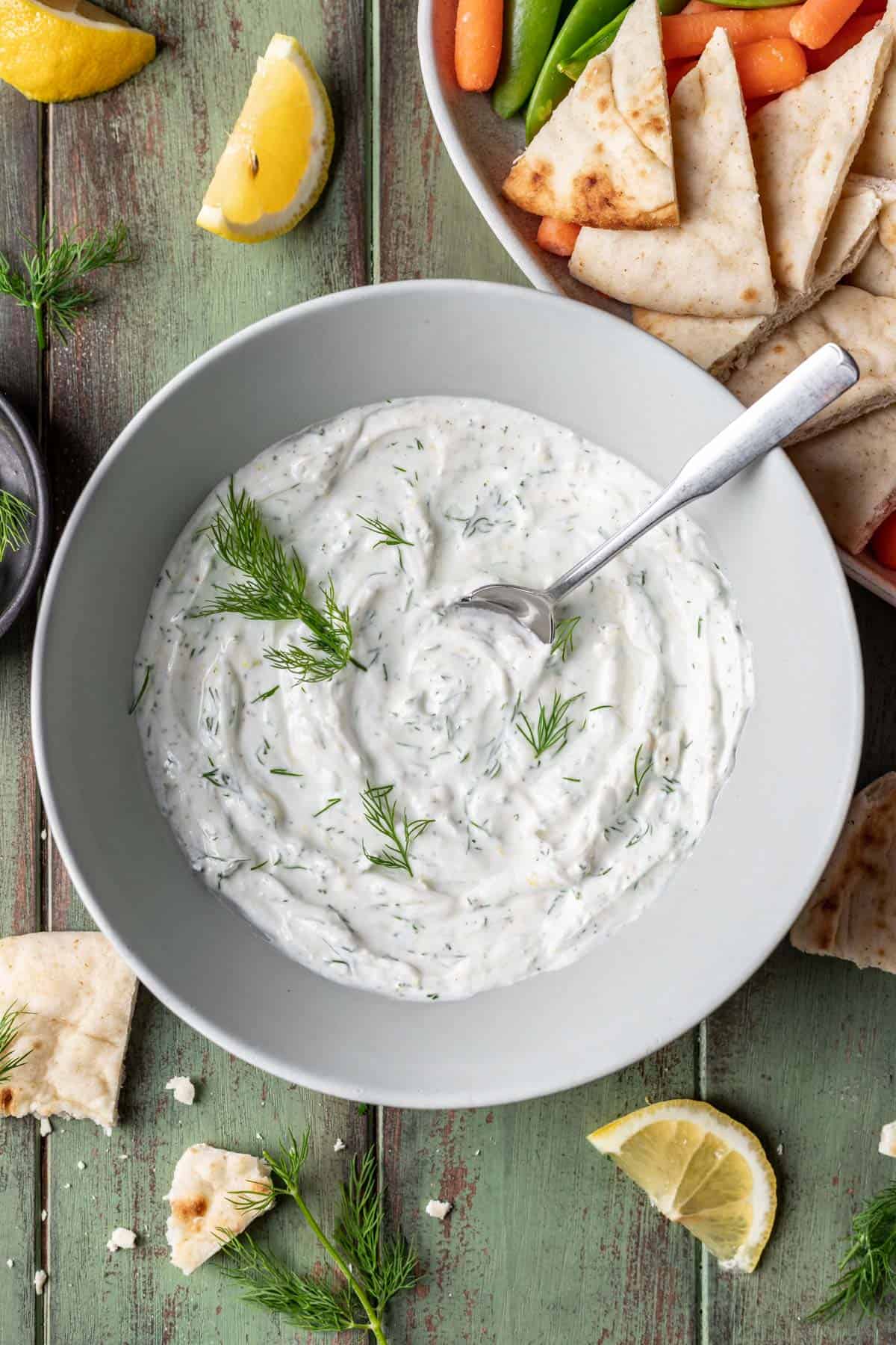 Lemon dill yogurt sauce in a serving bowl with pita and vegetables next to it.