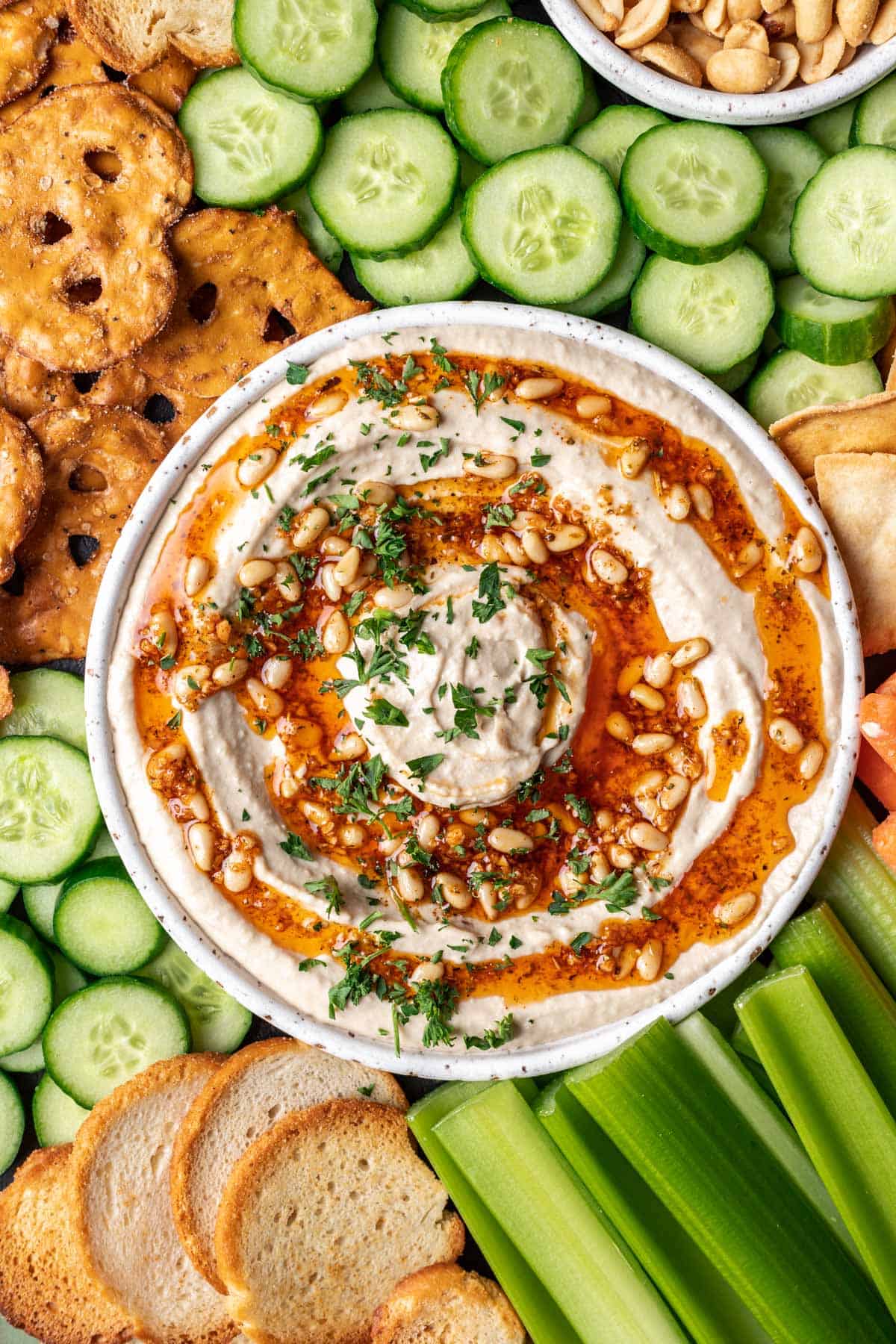 Pine nut hummus on a serving platter with fresh vegetables, pretzels, and chips.