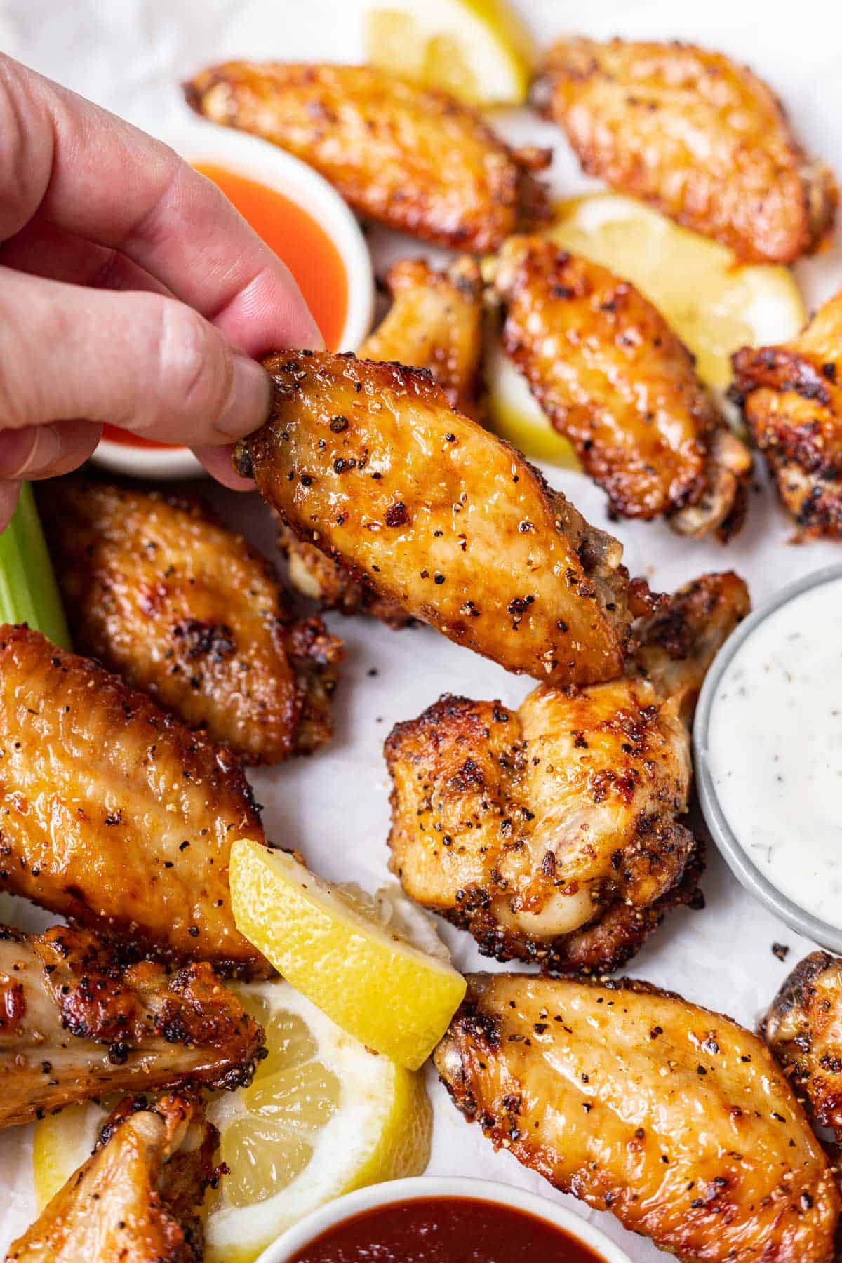 A hand picking up an air fryer chicken wing from a serving platter.