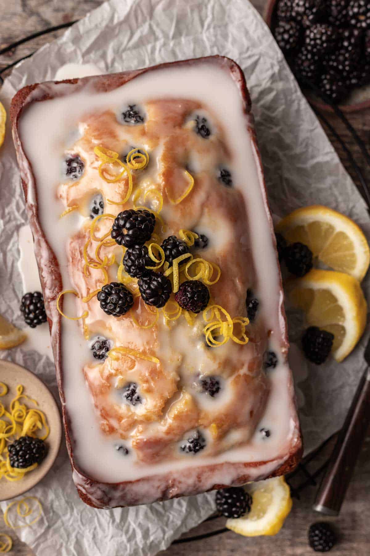 A glazed loaf of blackberry lemon bread on a cooling rack topped with blackberries and lemon zest.