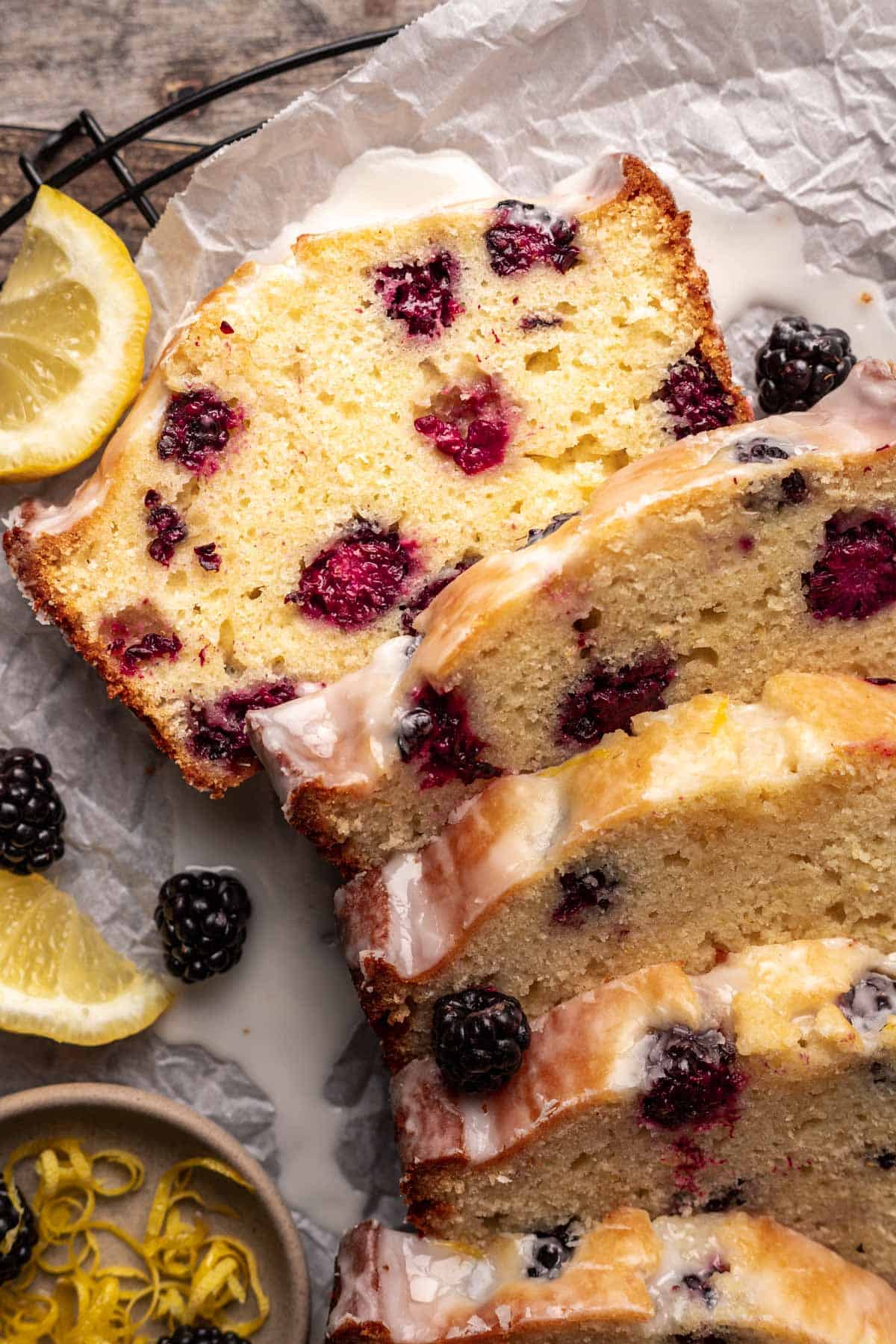 Sliced blackberry lemon bread on a cooling rack with lemon wedges.