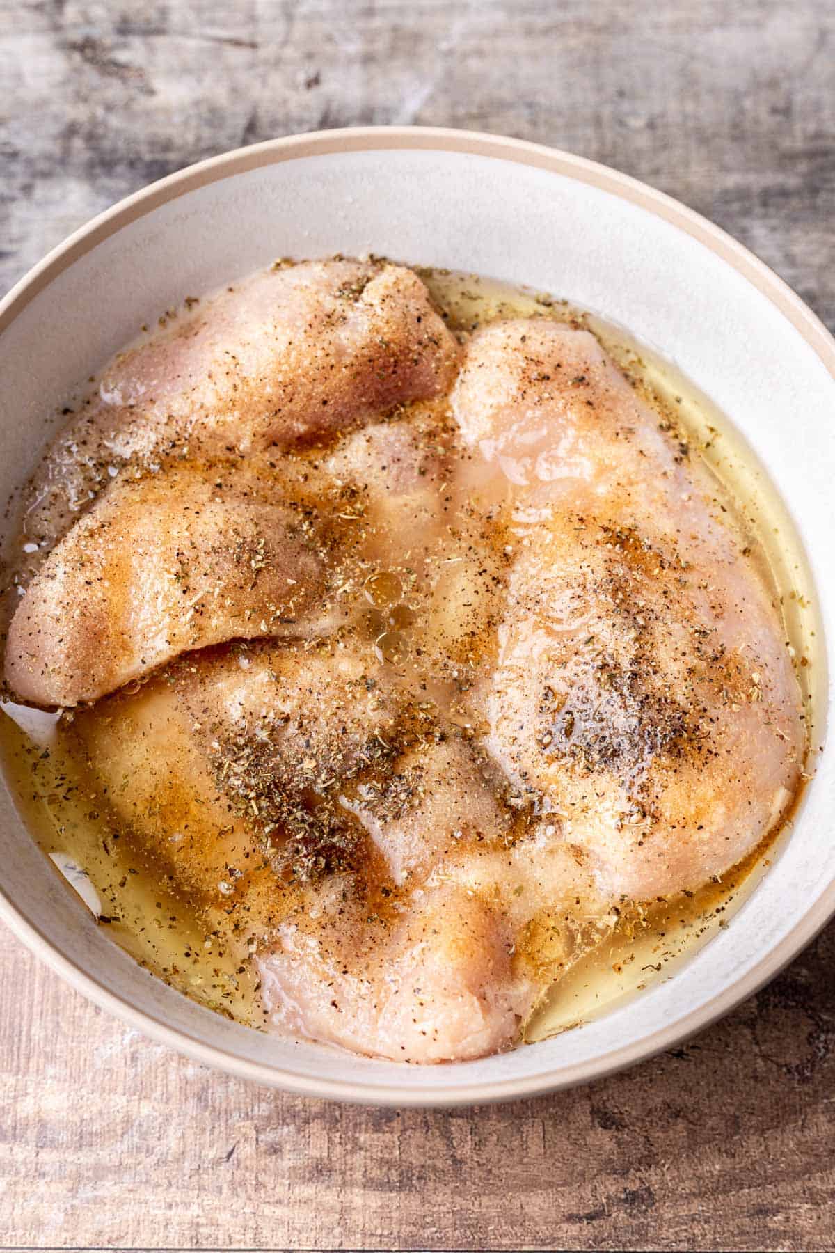 Raw chicken in a bowl with seasonings, oil, lemon juice, and maple syrup.
