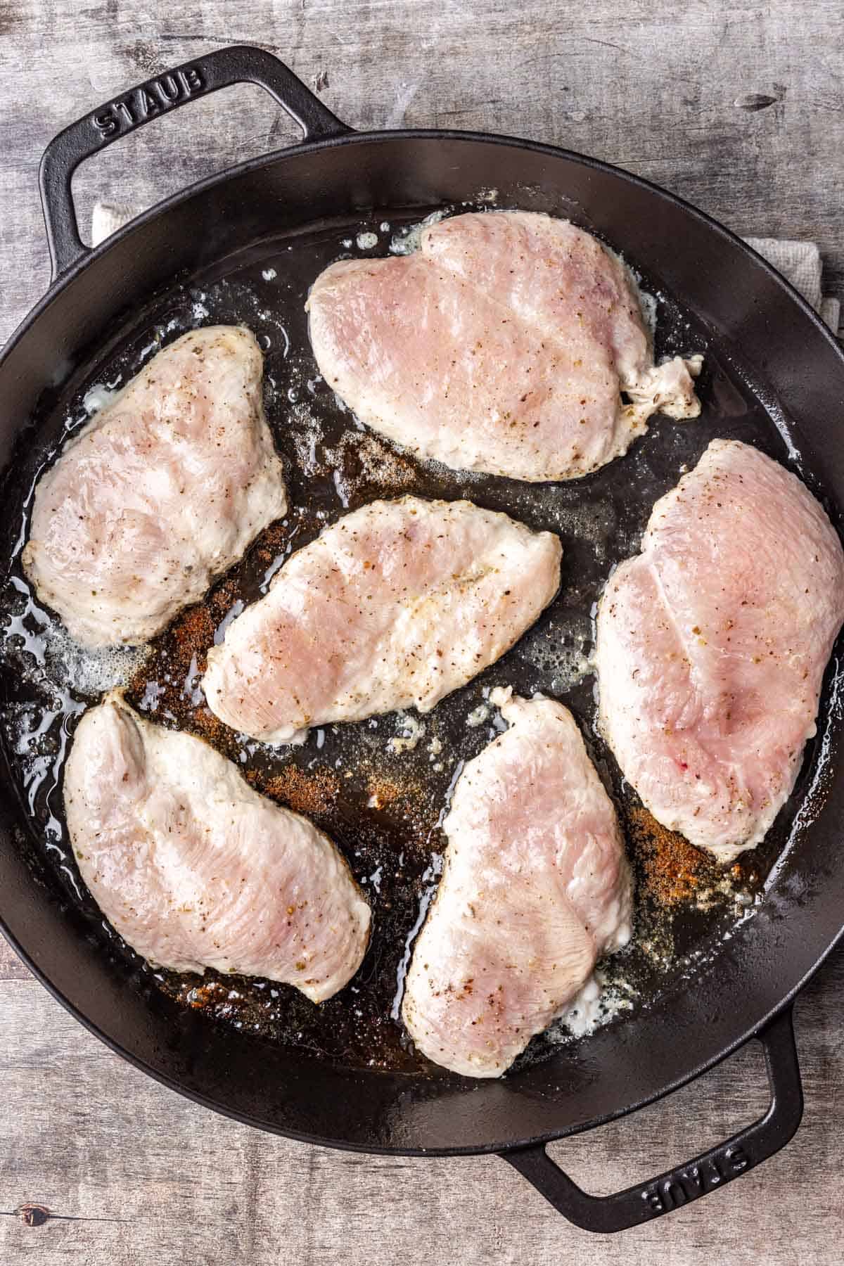 Raw chicken cooking in a cast iron skillet.