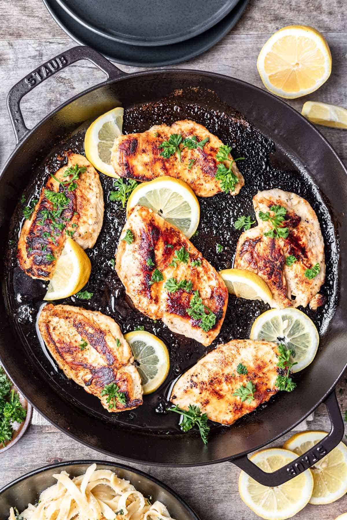 Chicken breasts cooked in a cast iron skillet, garnished with lemon slices and parsley.