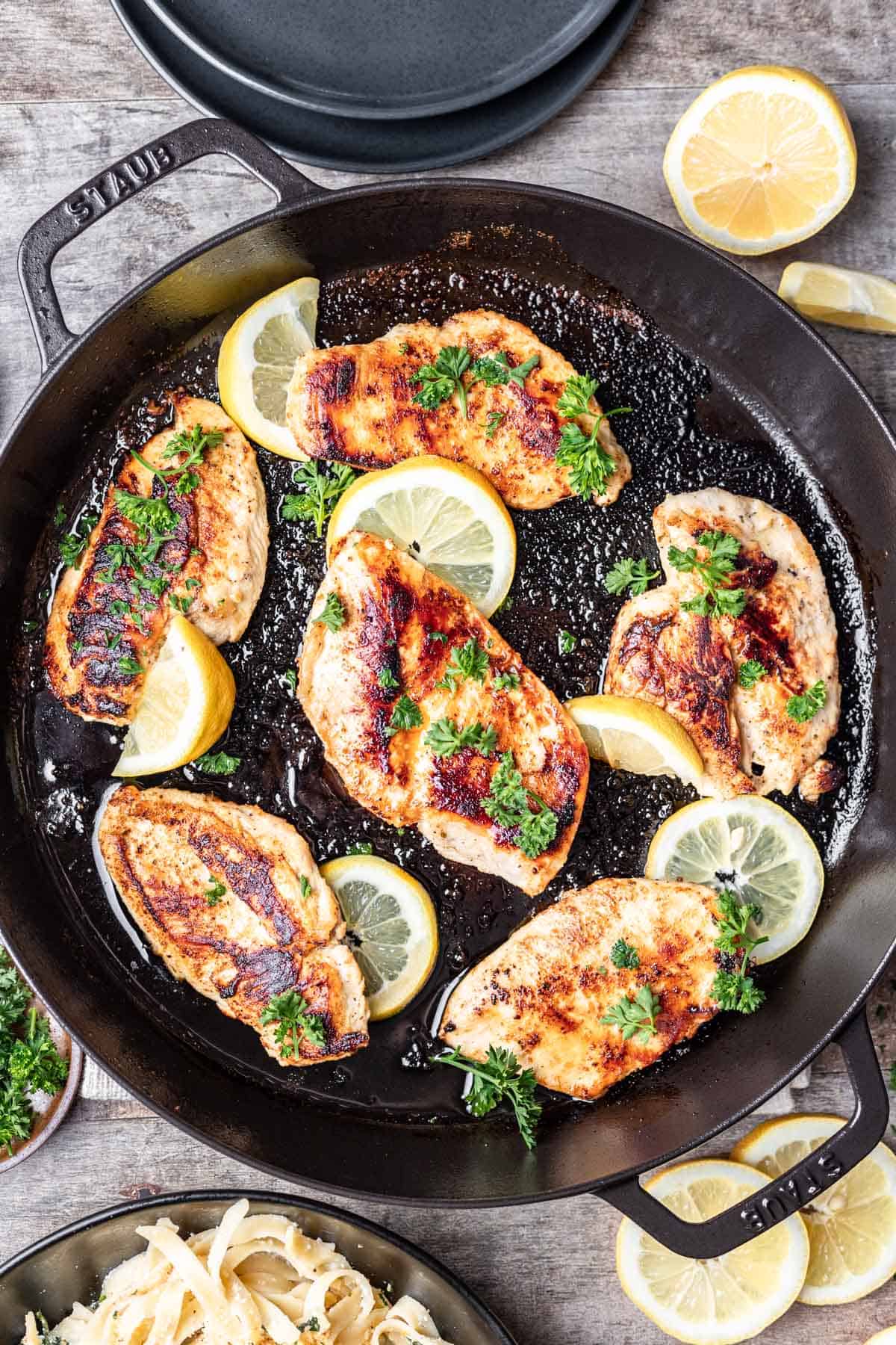 Chicken breasts cooked in a cast iron skillet, garnished with lemon slices and parsely.