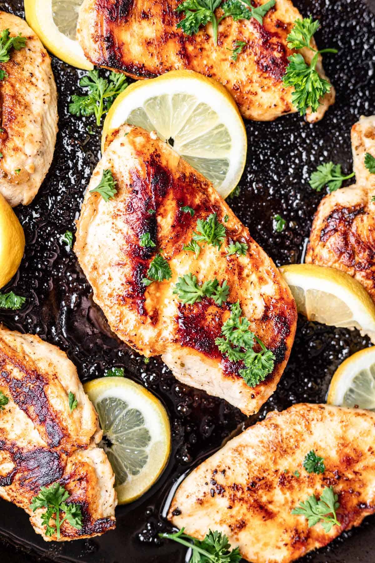 A chicken breast with a golden brown exterior garnished with fresh parsley in a cast iron skillet.