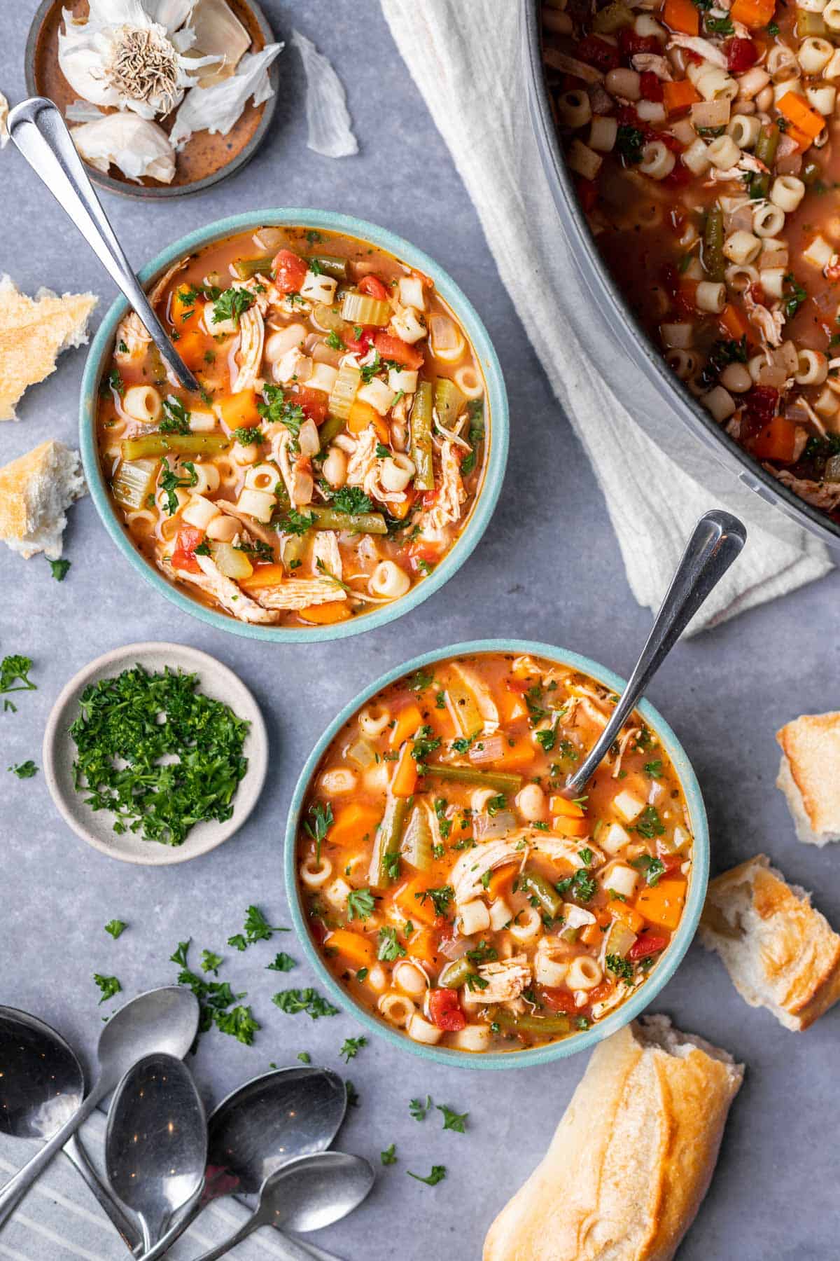 Chicken minestrone soup in two bowls with a side of french bread and fresh chopped parsley.