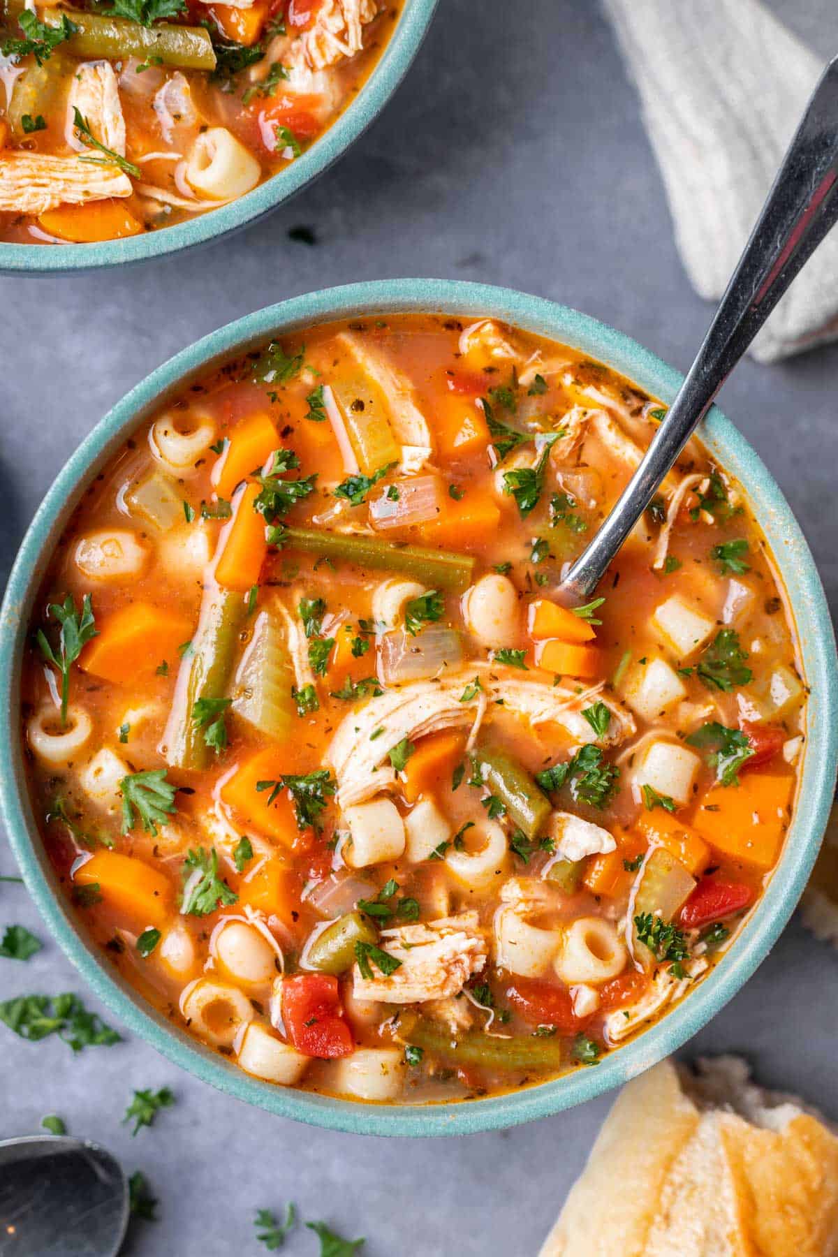 Chicken minestrone soup in a blue bowl with a spoon.