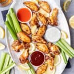 Air fryer lemon pepper wings on a platter with hot sauce, ranch, and bbq sauce.