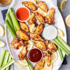 Air fryer lemon pepper wings on a platter with hot sauce, ranch, and bbq sauce.