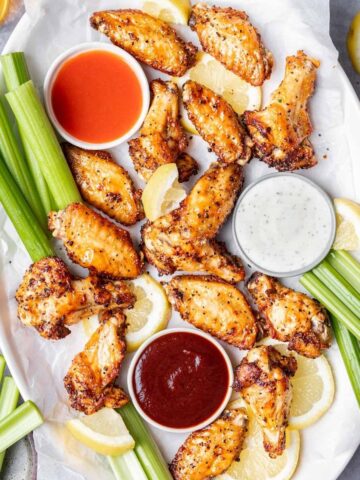 Air fryer lemon pepper wings on a platter with hot sauce, ranch, and bbq sauce.