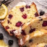 Blackberry lemon bread sliced on a cooling rack with lemons around it.