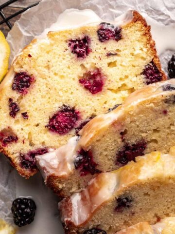 Blackberry lemon bread sliced on a cooling rack with lemons around it.