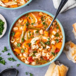 A bowl of minestrone soup with a spoon and crusty bread on the side.