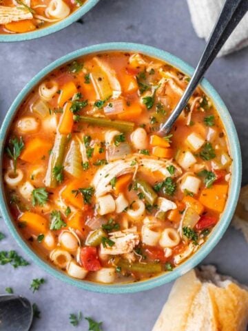 A bowl of minestrone soup with a spoon and crusty bread on the side.