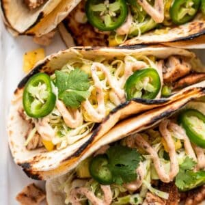 Jerk chicken tacos garnished with jalapeño slices and cilantro on a serving dish.