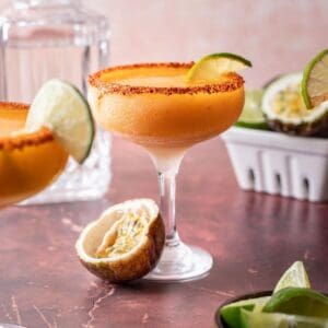 Passion fruit margarita in a coupe glass with a lime slice and a halved passion fruit.