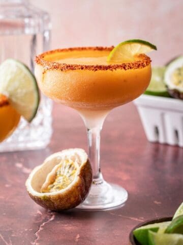 Passion fruit margarita in a coupe glass with a lime slice and a halved passion fruit.