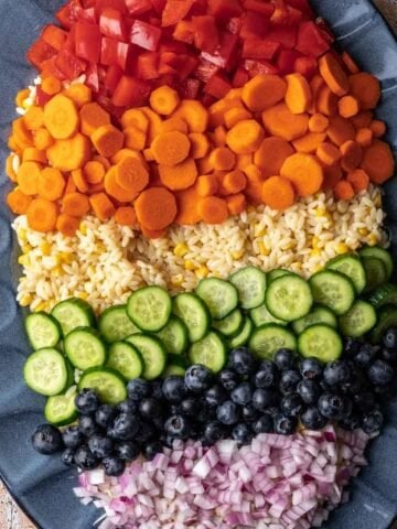 Rainbow orzo salad with pesto on a blue serving platter.