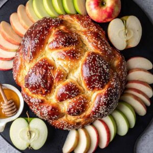 Round challah (for rosh hashanah) surrounded by sliced apples and honey.