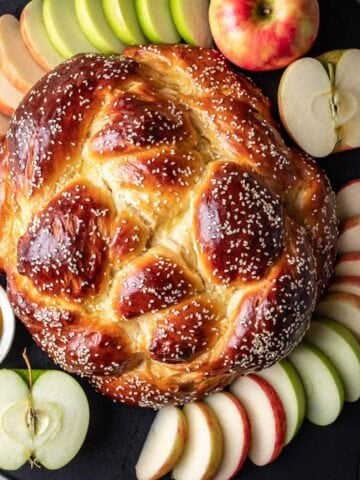 Round challah (for rosh hashanah) surrounded by sliced apples and honey.