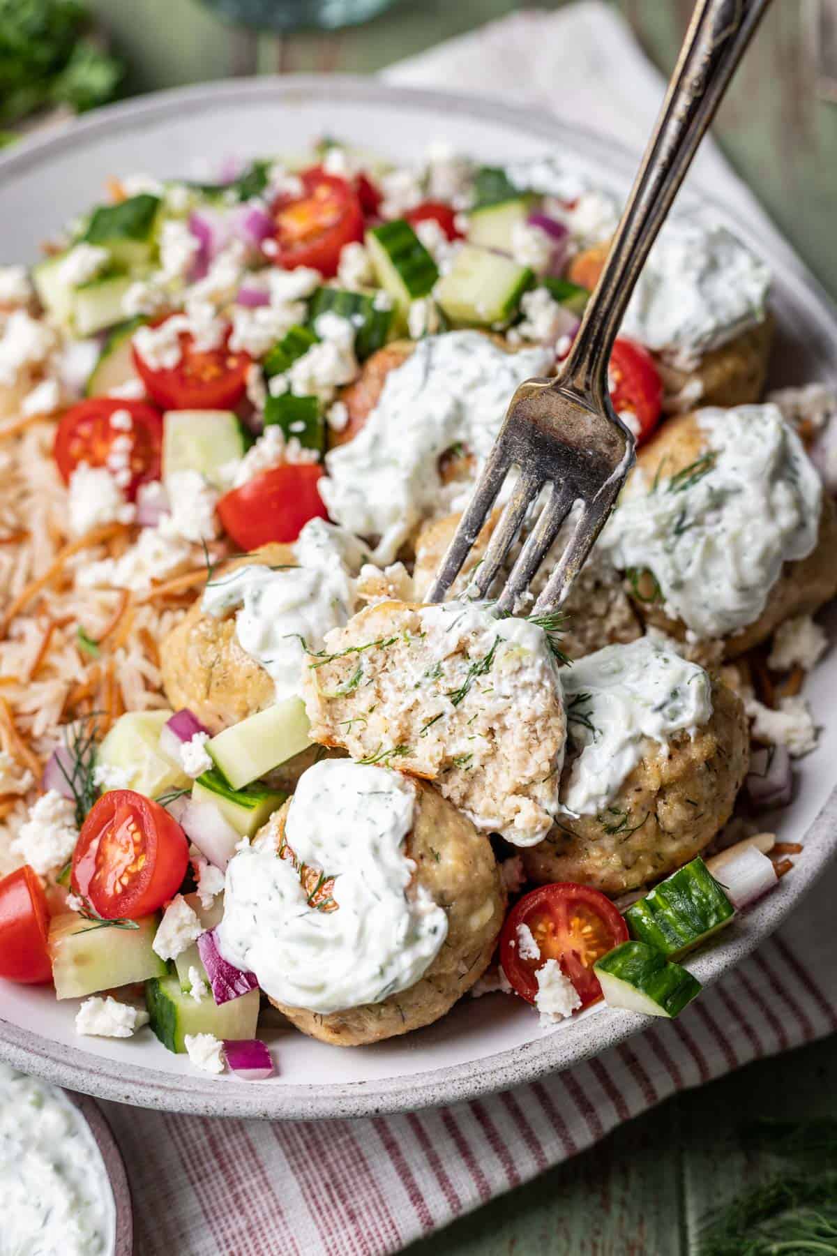 A fork cutting a greek chicken meatball in half to show the inside.