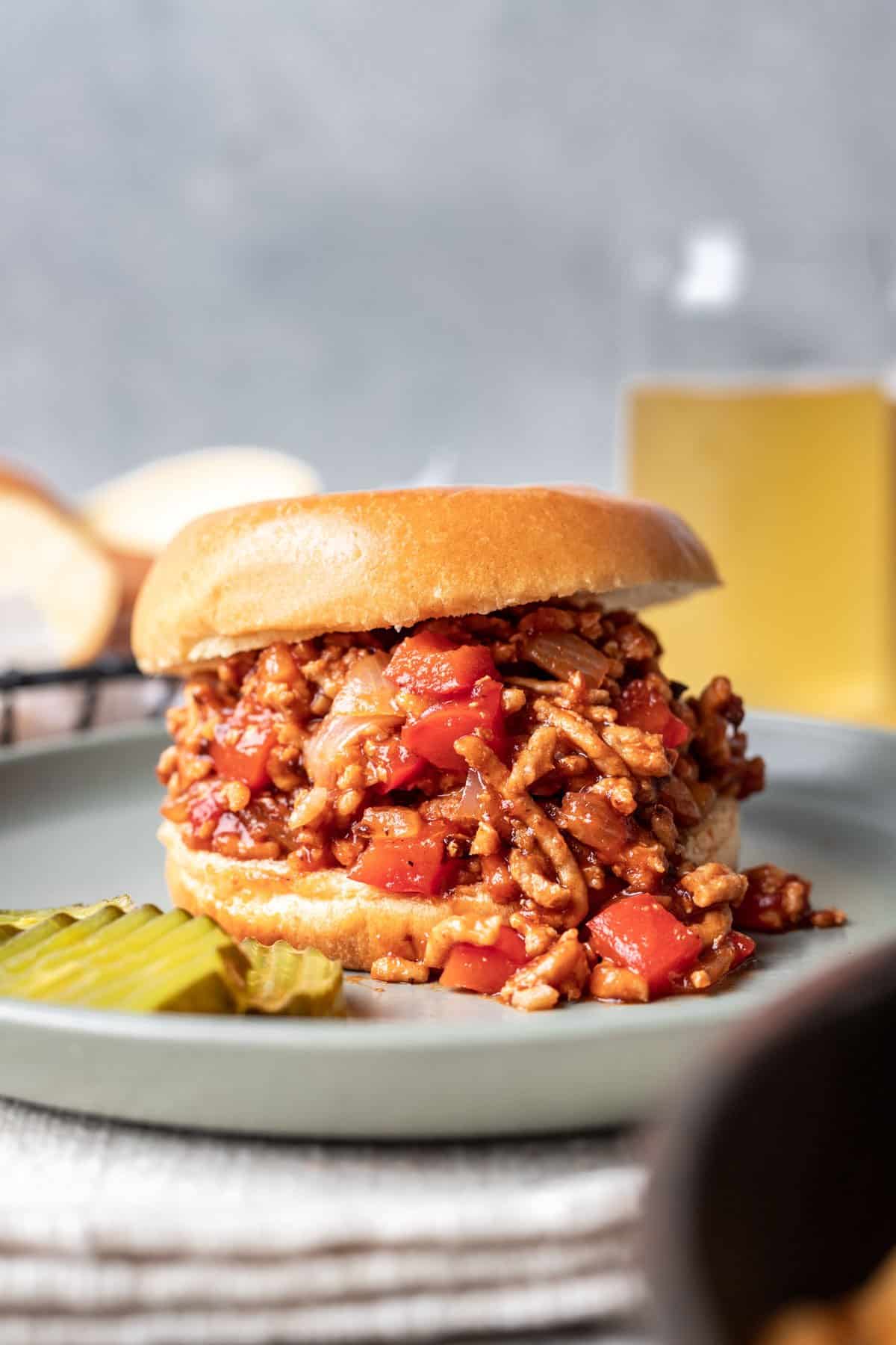 Ground chicken sloppy joes on a brioche bun with a side of pickle chips.