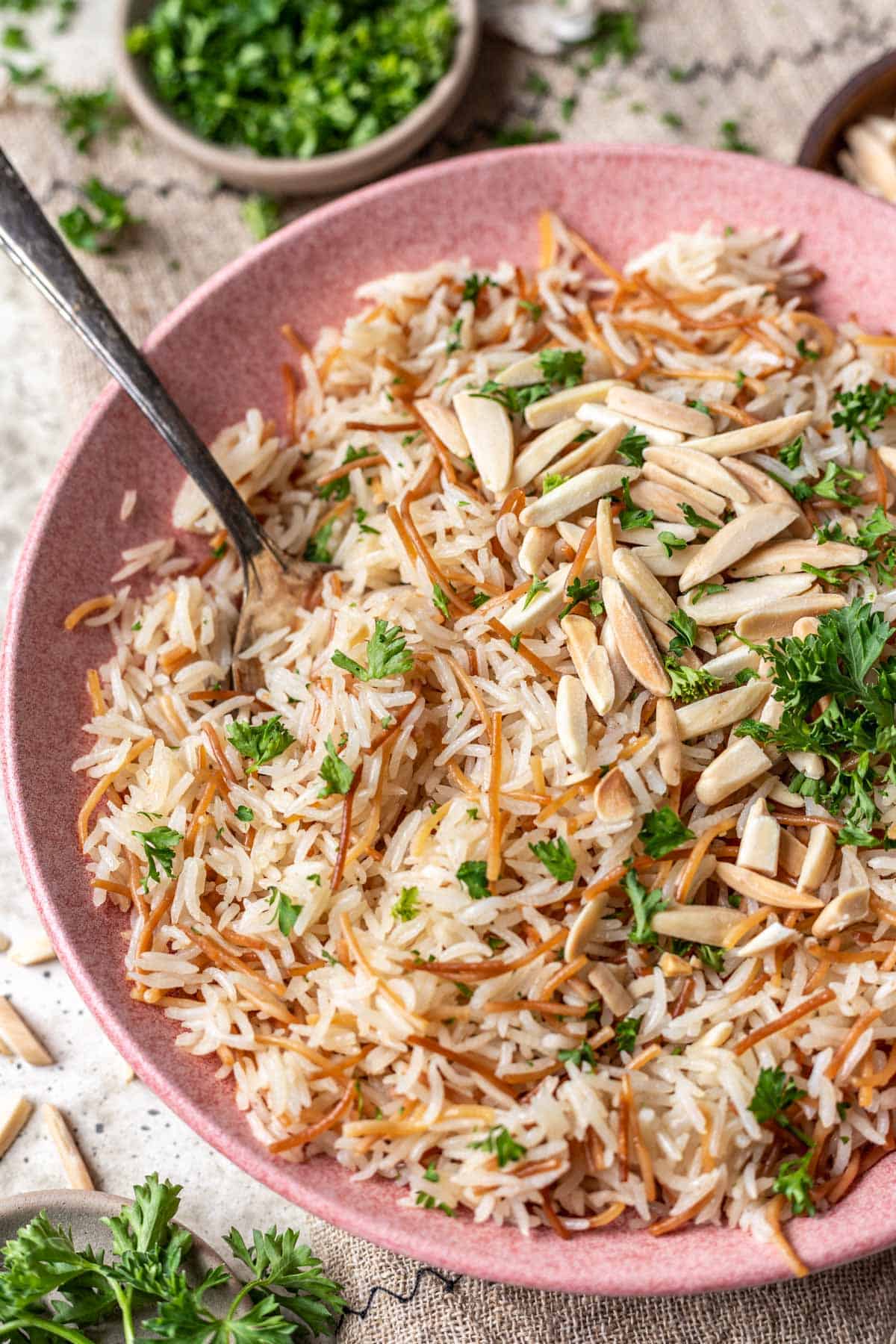 Instant pot rice pilaf in a serving bowl with a spoon, toasted almonds, and parsley.