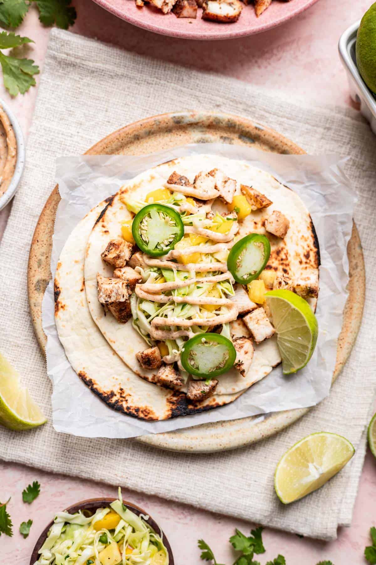 A jerk chicken taco assembled on a plate with chicken, slaw, and aioli.