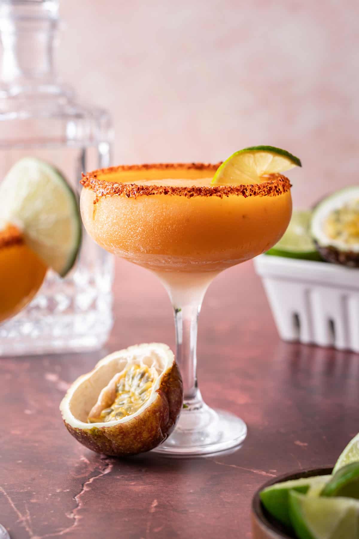 Passion fruit margarita with a tajin rim, garnished with a lime slice and a halved passion fruit on the side.