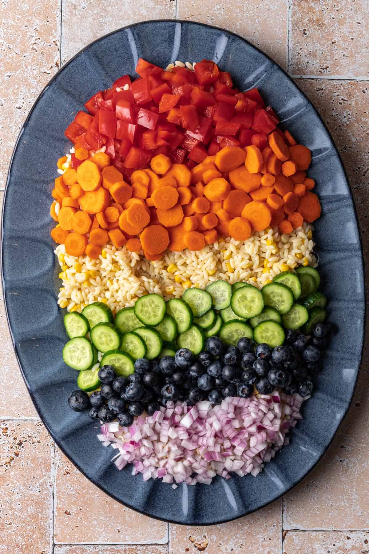 Orzo salad with rainbow ingredients displayed on a blue serving platter.