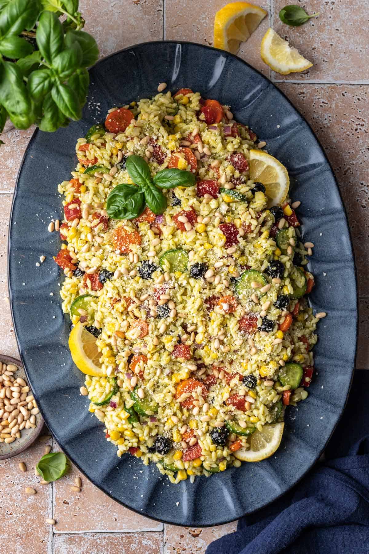 Rainbow orzo salad coated in pesto and topped with fresh basil, pine nuts, and parmesan cheese.