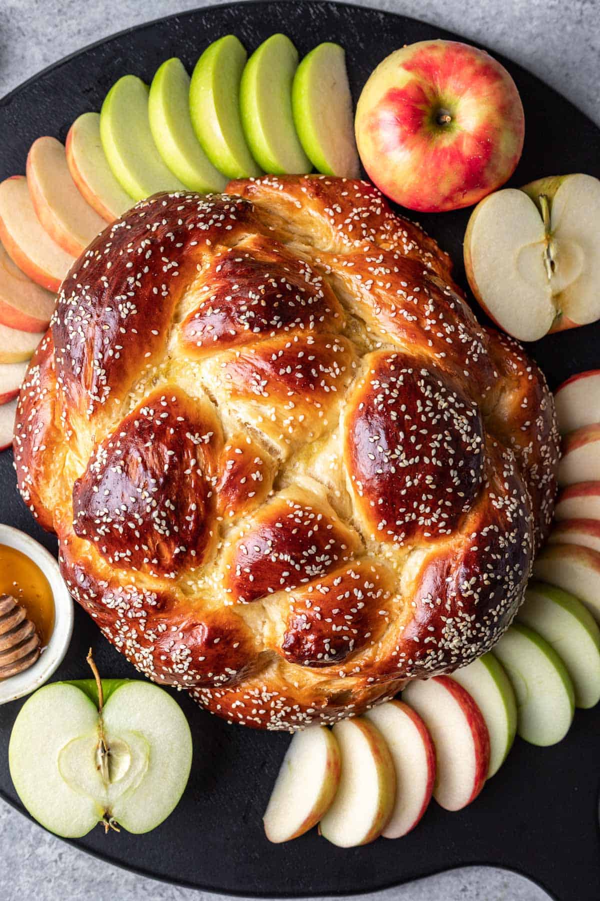 Round challah for rosh hashanah on a serving tray with sliced apples and honey.